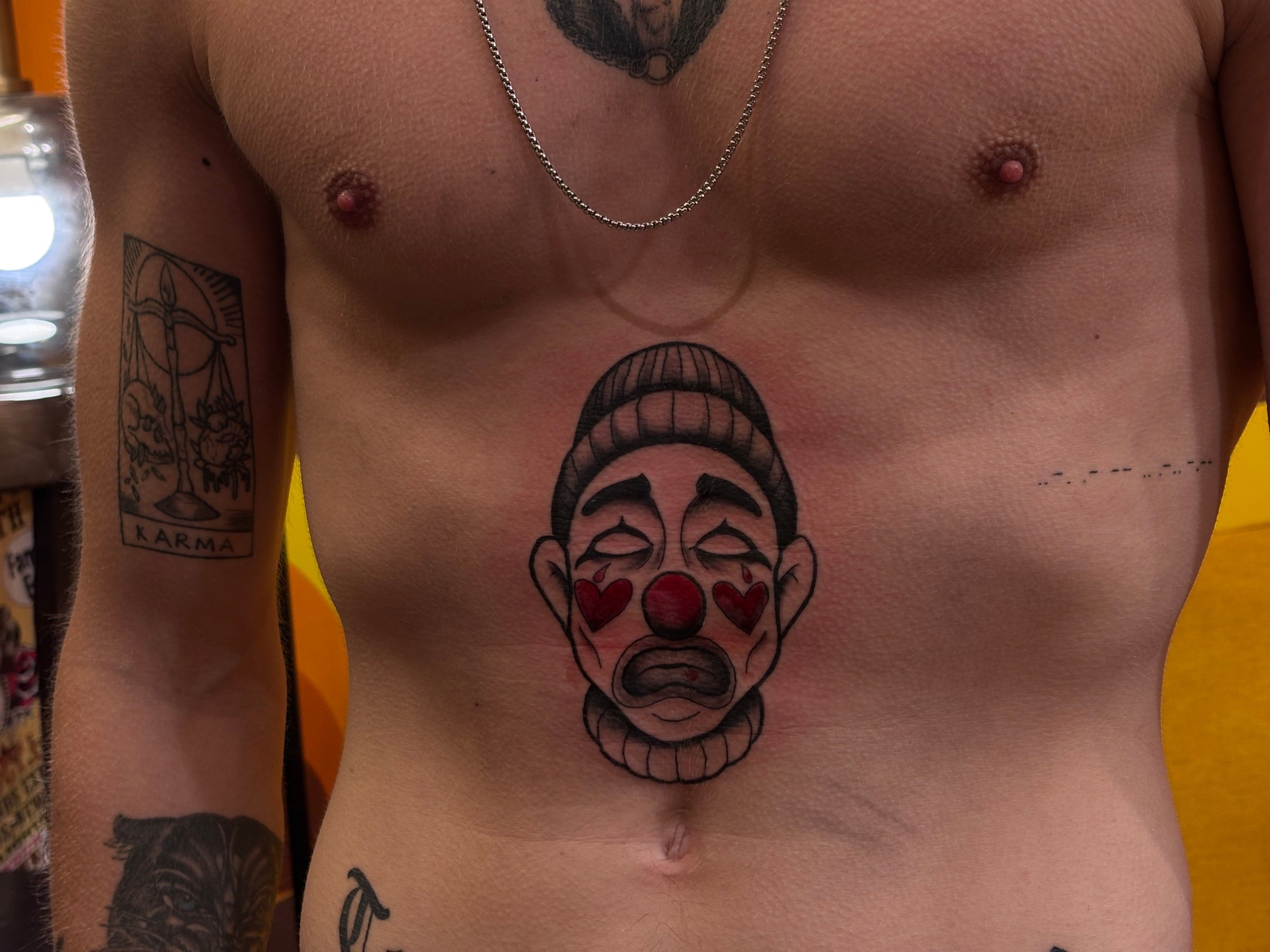 Tatouage en couleurs inspiré de l'univers traditionnel, représentant un clown mélancolique où les touches de rouge viennent contraster avec des ombrages en black & grey.